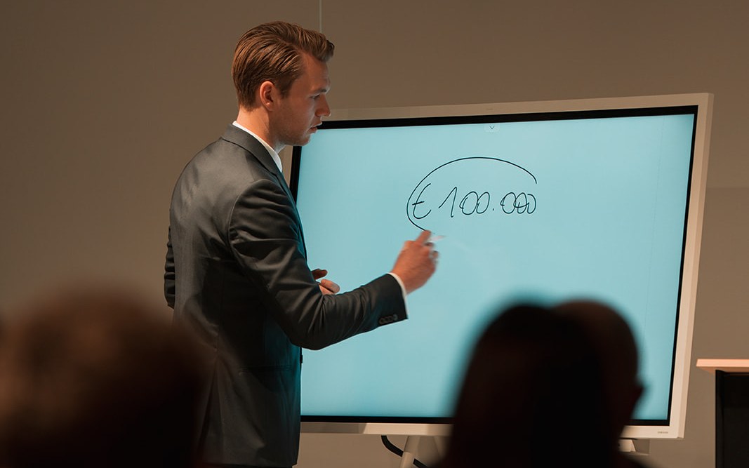 Spreker schrijft €100.000 op het scherm tijdens een Archer-workshop
